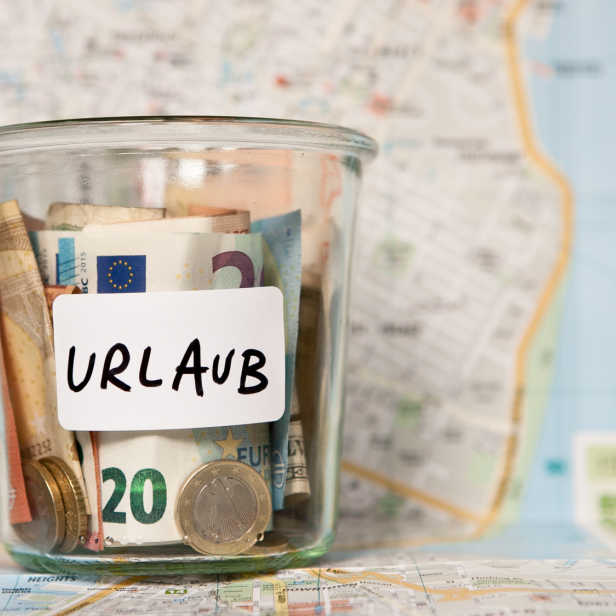 Ein Glas mit Geld und dem Wort „Urlaub“ steht auf einer Landkarte.