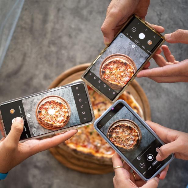 Mehrere Handys fotografieren eine Pizza auf einem Holzteller.