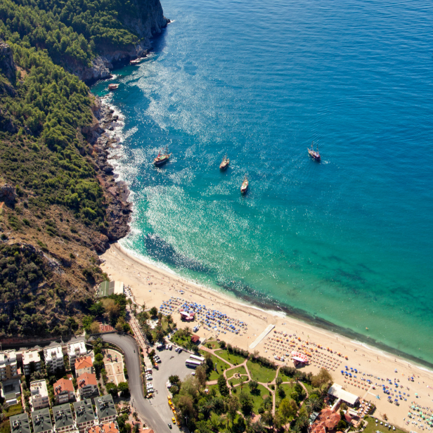 Luftaufnahme eines Strandes mit türkisfarbenem Wasser und mehreren Booten.