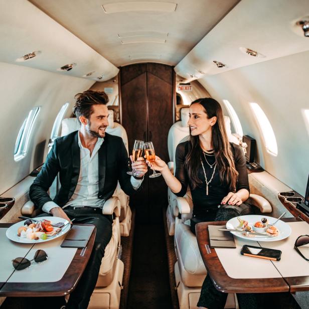 Ein Mann und eine Frau stoßen in einem Privatjet mit Champagner an.