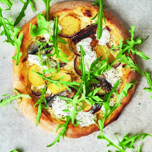 Eine Pizza mit Kartoffeln, Zwiebeln, Mozzarella und Rucola belegt.