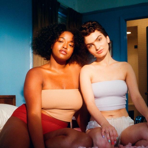 Zwei Frauen sitzen auf einem Bett mit einem rosa Fellteppich.