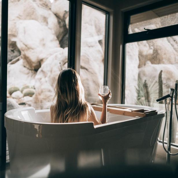 Eine Frau entspannt mit einem Getränk in der Badewanne mit Blick auf Felsen.