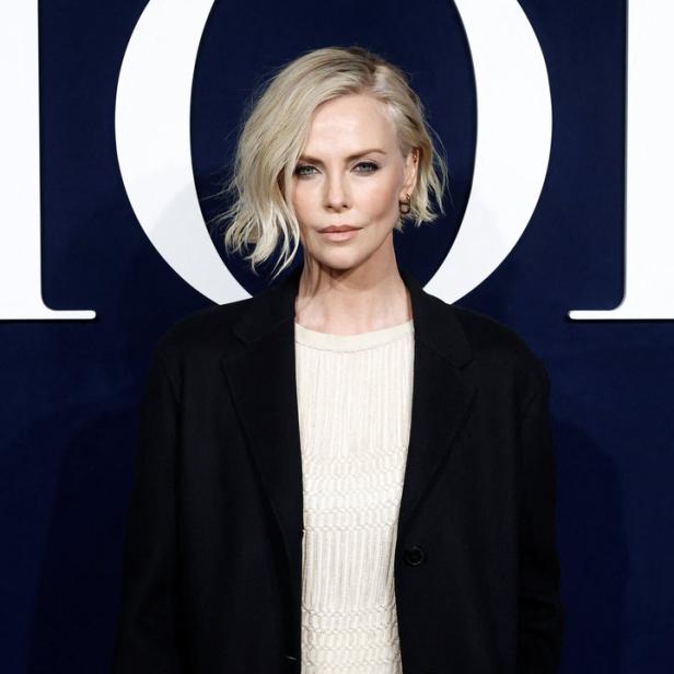 Charlize Theron posiert vor einem Dior-Logo.