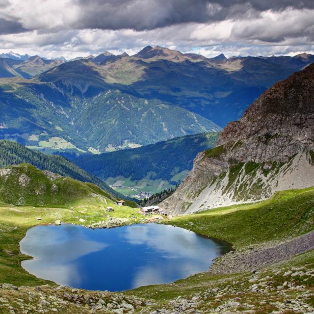Ein Bergsee spiegelt den Himmel und die umliegende grüne Landschaft wider.