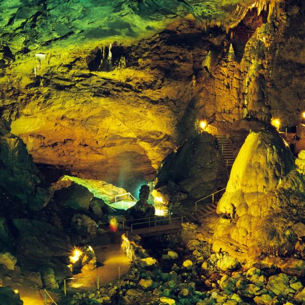 Beleuchtete Tropfsteinhöhle mit Treppen und einem kleinen Übergang.