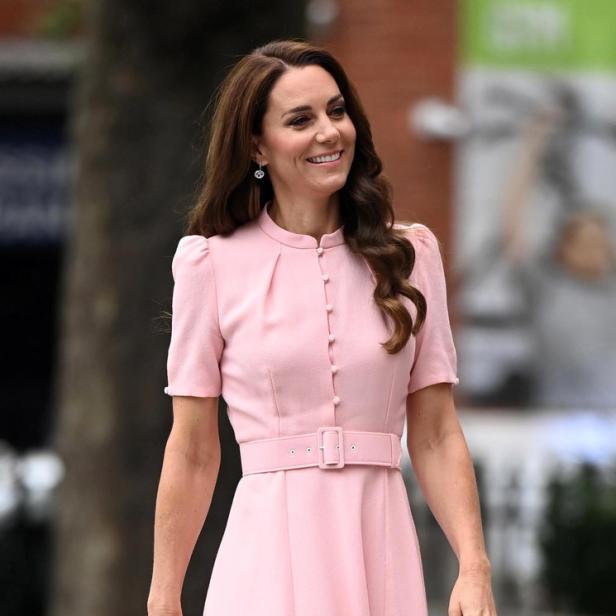 Kate Middleton trägt ein rosa Kleid mit Gürtel und lächelt.