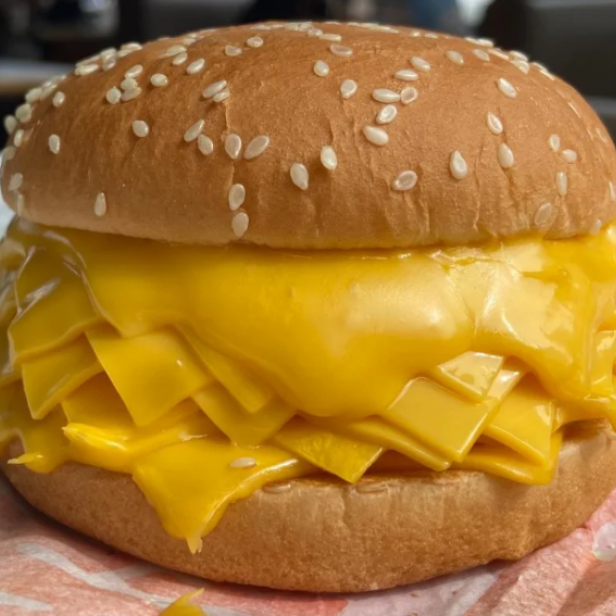 Ein Cheeseburger mit sehr viel Käse liegt auf einem Papier.