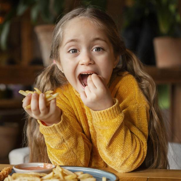 Ein Mädchen isst Pommes Frites mit großem Appetit.