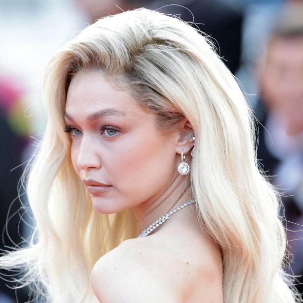 Gigi Hadid mit blonden, gewellten Haaren und auffälligem Schmuck auf einem roten Teppich.