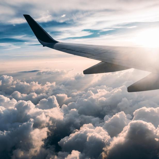 Blick aus einem Flugzeugfenster auf eine Wolkendecke bei Sonnenaufgang.
