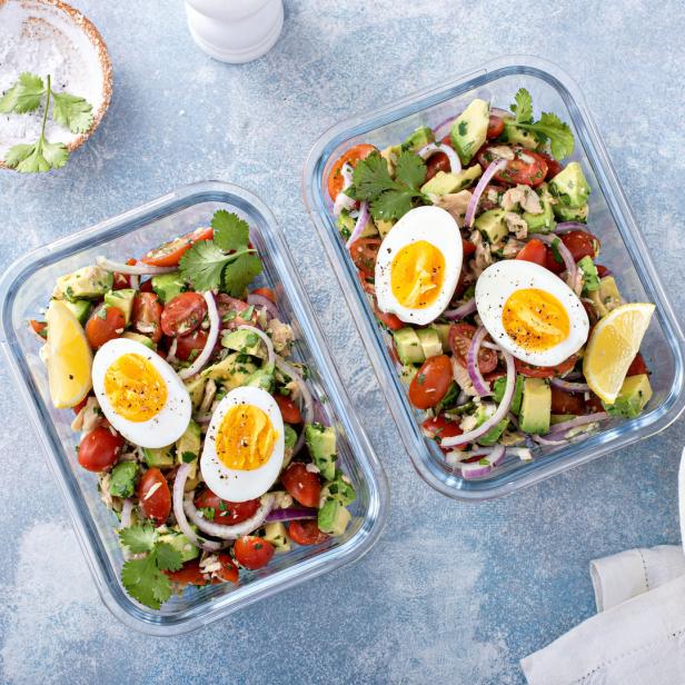 Zwei Salatschüsseln mit Avocado, Tomaten, Eiern und Zitrone stehen auf einem Tisch.
