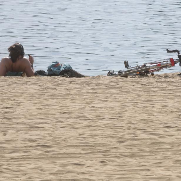Eine Frau liegt am Strand der Neuen Donau in Wien, neben ihr ein Fahrrad.