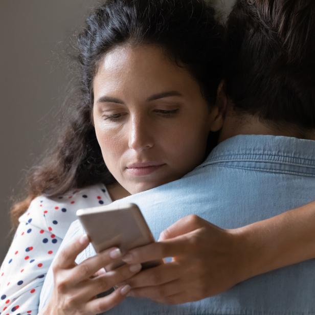 Eine Frau umarmt einen Mann und schaut auf ihr Handy.