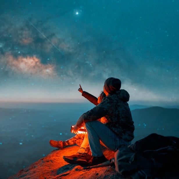Eine Person sitzt auf einem Felsen und blickt in den Sternenhimmel.