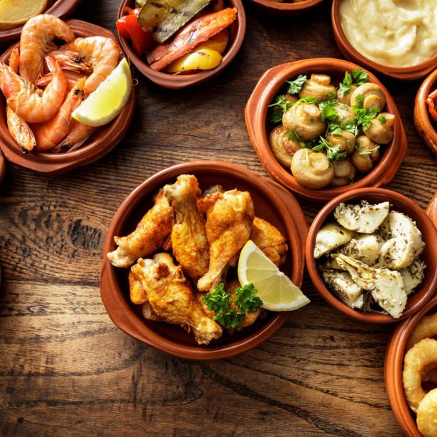 Verschiedene Tapas-Gerichte in kleinen Schalen auf einem Holztisch.