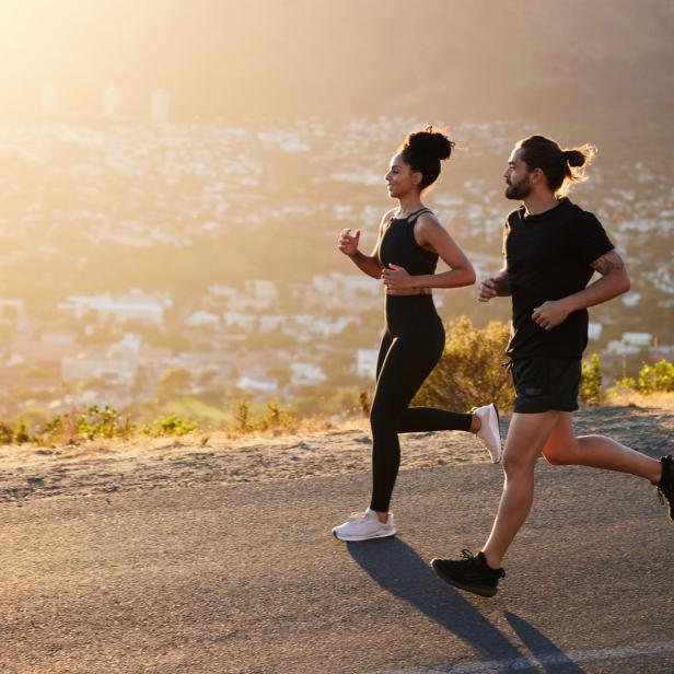 Eine Frau und ein Mann joggen auf einer Straße mit Blick auf eine Stadt im Hintergrund.