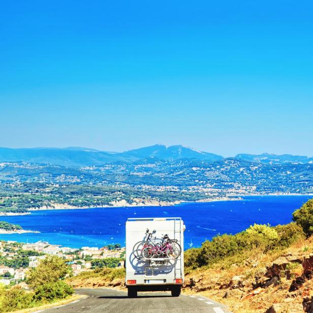 Ein Wohnmobil fährt auf einer Straße mit Blick auf das Meer und die Berge.