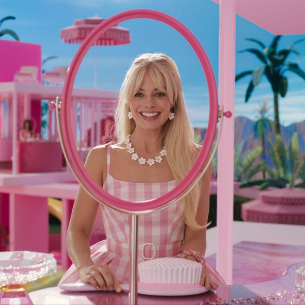Margot Robbie als Barbie vor ihrem pinkfarbenen Haus mit Pool und Palmen.