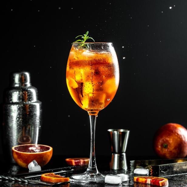Ein Aperol Spritz wird mit einer Orangenscheibe und Rosmarin garniert.
