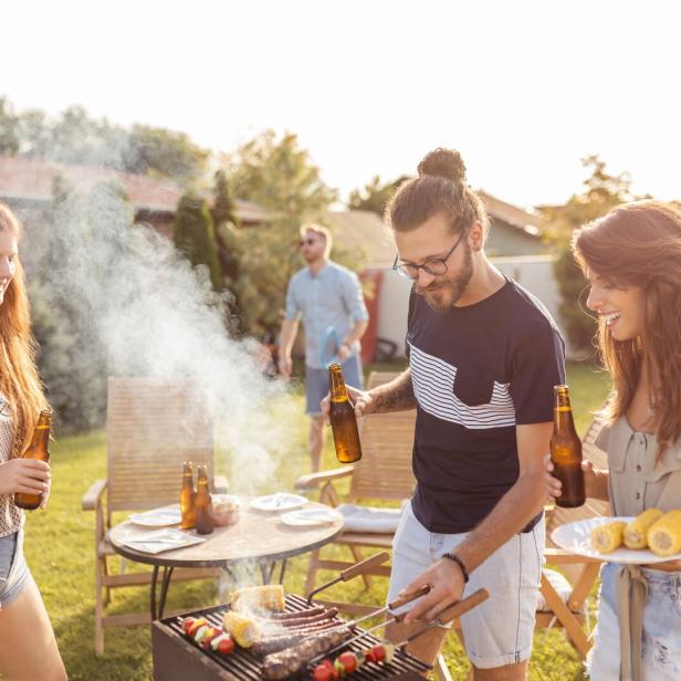Eine Gruppe von Freunden grillt im Garten und genießt den sonnigen Tag.