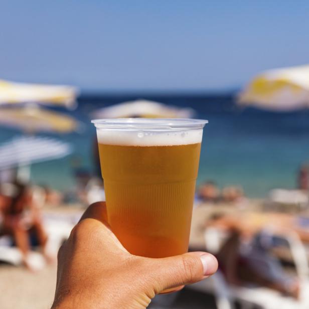 Ein Mann hält ein Bier am Strand in der Hand.