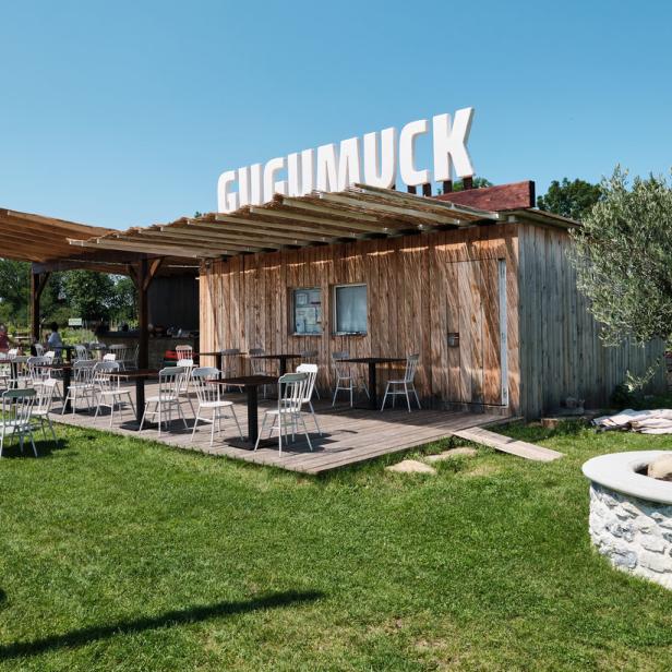 Das Restaurant „Gugumuck“ mit Tischen und Stühlen im Freien an einem sonnigen Tag.