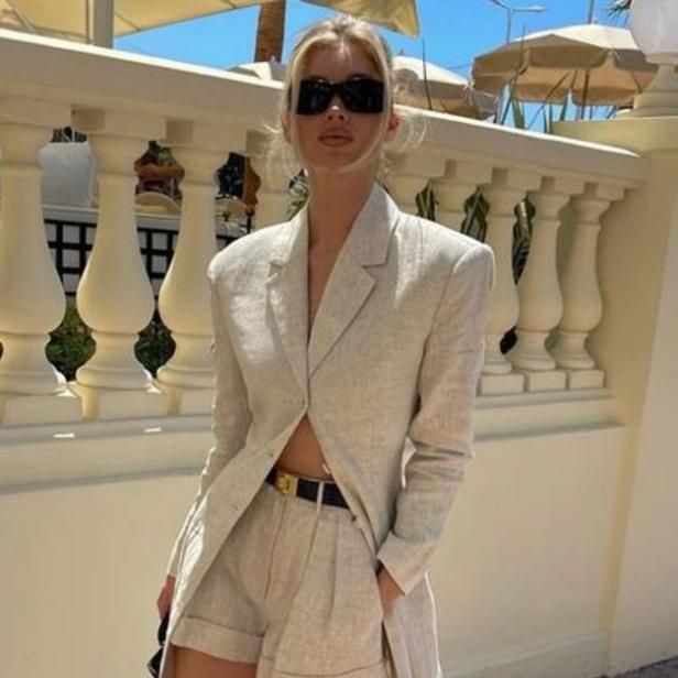 Eine blonde Frau trägt einen beigen Blazer und Shorts mit schwarzen Loafers.