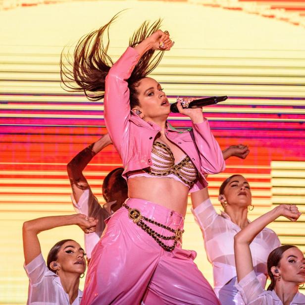 Rosalía tritt in einem pinkfarbenen Outfit mit Tänzern auf einer Bühne auf.