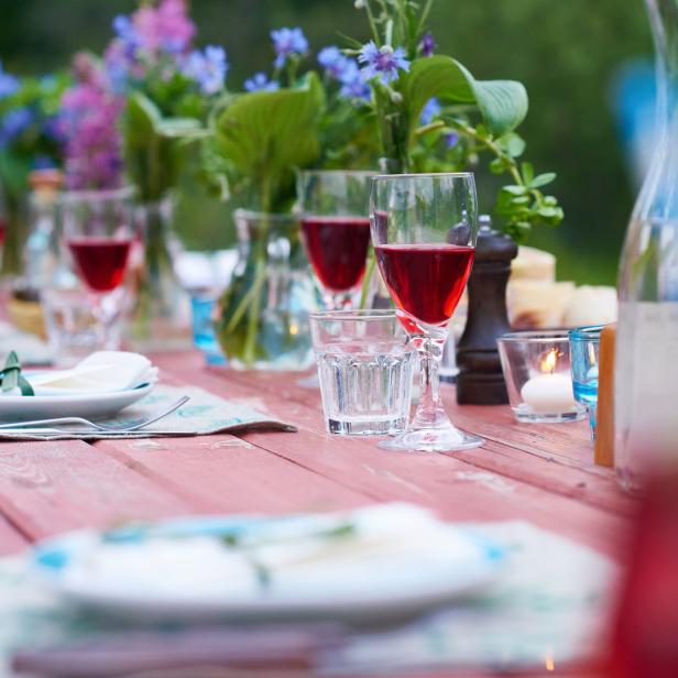 Ein gedeckter Holztisch mit Blumen, Tellern, Gläsern und Getränken für eine Feier im Freien.