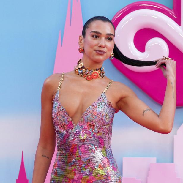 Dua Lipa posiert in einem bunten Kleid auf einem pinkfarbenen Teppich.