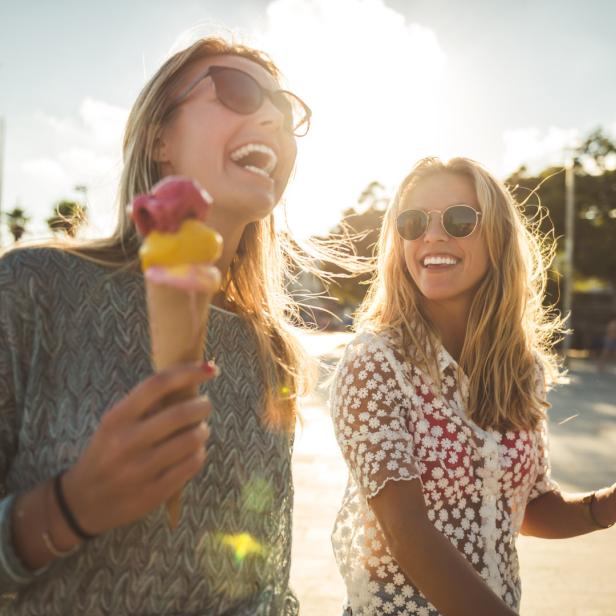 Zwei junge Frauen lachen und halten Eiswaffeln in der Hand.