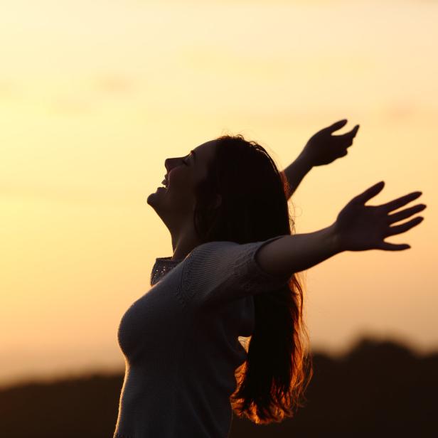 Eine Frau steht mit offenen Armen vor einem orangefarbenen Himmel.