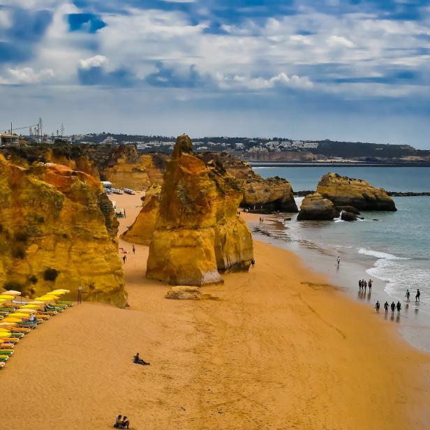 Blick auf den Strand Praia do Camilo in Lagos, Portugal, mit gelben Felsformationen und Menschen.