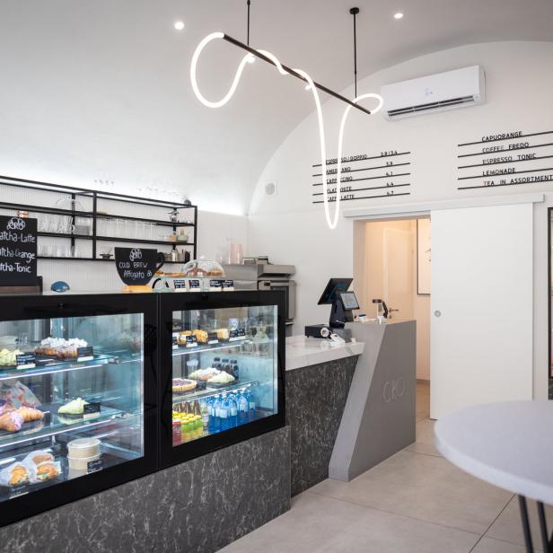 Innenansicht eines modernen Cafés mit Theke, Kuchenvitrine und Menütafel.
