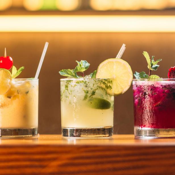 Drei verschiedene Cocktails stehen auf einer Bar, garniert mit Früchten und Minze.