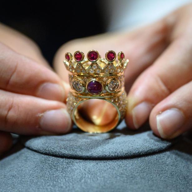 Ein goldener Ring in Form einer Krone mit Rubinen wird von Händen gehalten.
