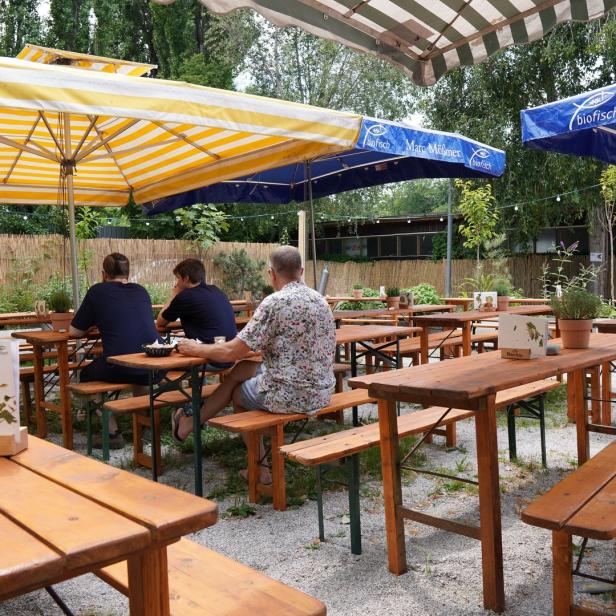 Ein Biergarten mit Holztischen und Bänken unter gestreiften Sonnenschirmen.