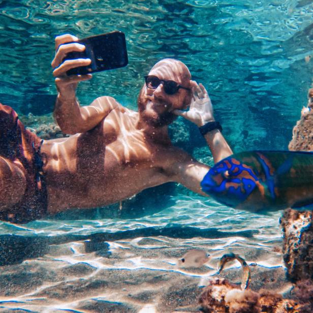 Ein Mann macht ein Unterwasser-Selfie mit einem bunten Fisch.
