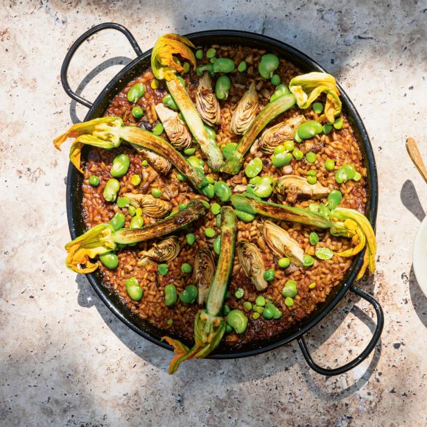 Paella mit Artischocken, Zucchiniblüten und Saubohnen, serviert mit einem Dip.
