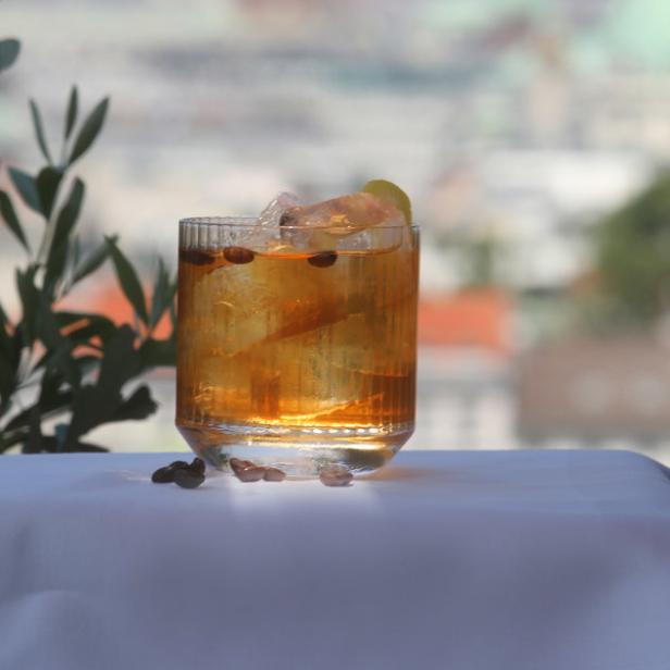 Ein Cocktail mit Eis und einer Zitronenscheibe vor einer Stadtkulisse.