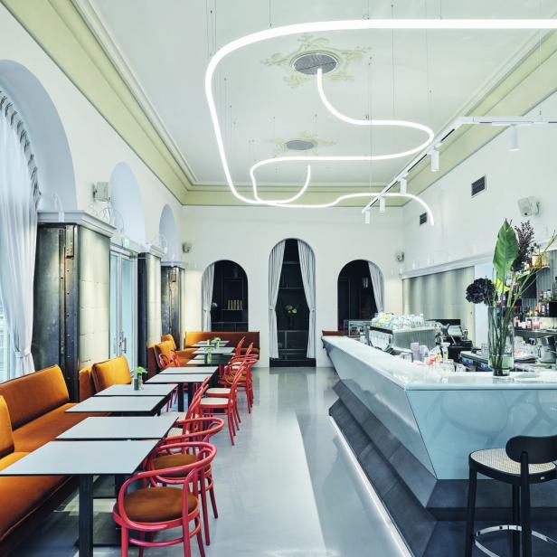Innenansicht eines modernen Cafés mit orangefarbenen Sitzbänken und Stühlen sowie einer Bar.