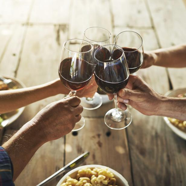 Mehrere Personen stoßen mit Rotwein an einem Holztisch an.
