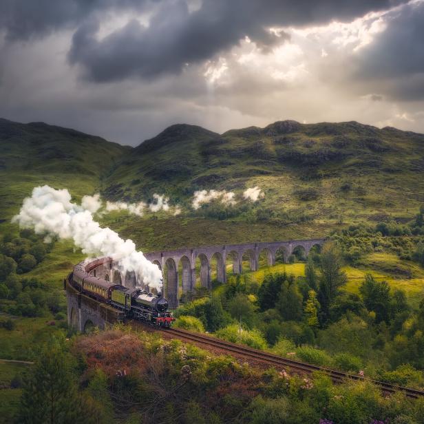 Ein Dampfzug fährt über das Glenfinnan-Viadukt in einer grünen Hügellandschaft.