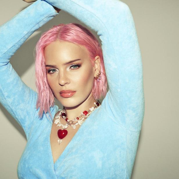 Anne-Marie posiert mit pinken Haaren und blauem Oberteil für ein Foto.