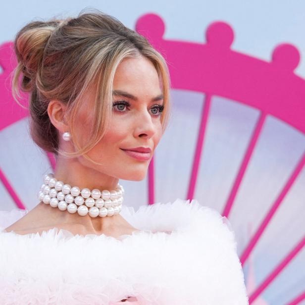 Margot Robbie mit Perlenkette und weißem Kleid vor einem rosa Riesenrad.