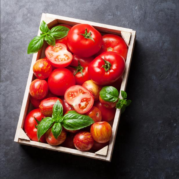 Eine Holzkiste gefüllt mit Tomaten und Basilikumblättern.