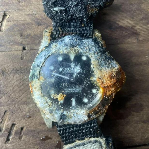 Eine stark beschädigte Rolex Submariner-Uhr liegt auf einer Holzoberfläche.