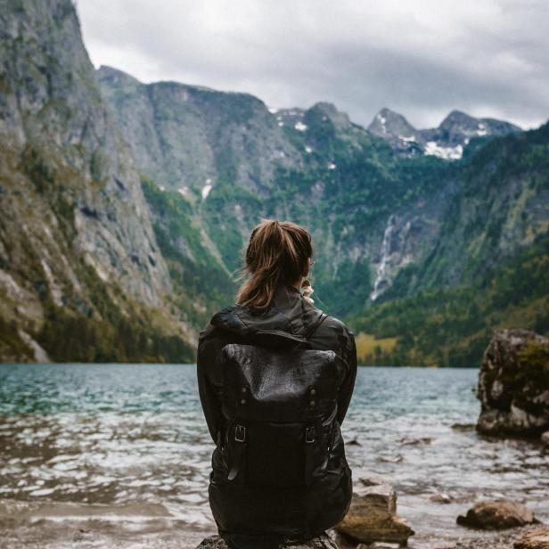 Eine Frau mit Rucksack sitzt am Ufer eines Bergsees.