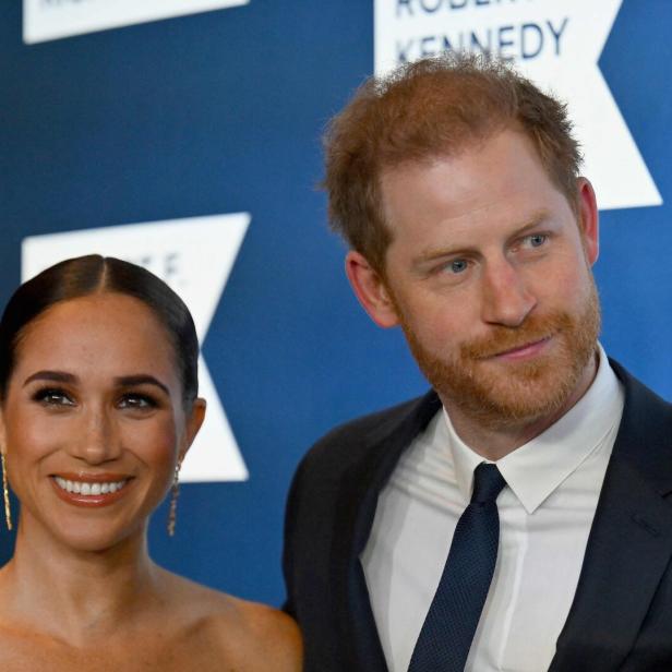 Meghan und Harry posieren vor einem blauen Hintergrund.